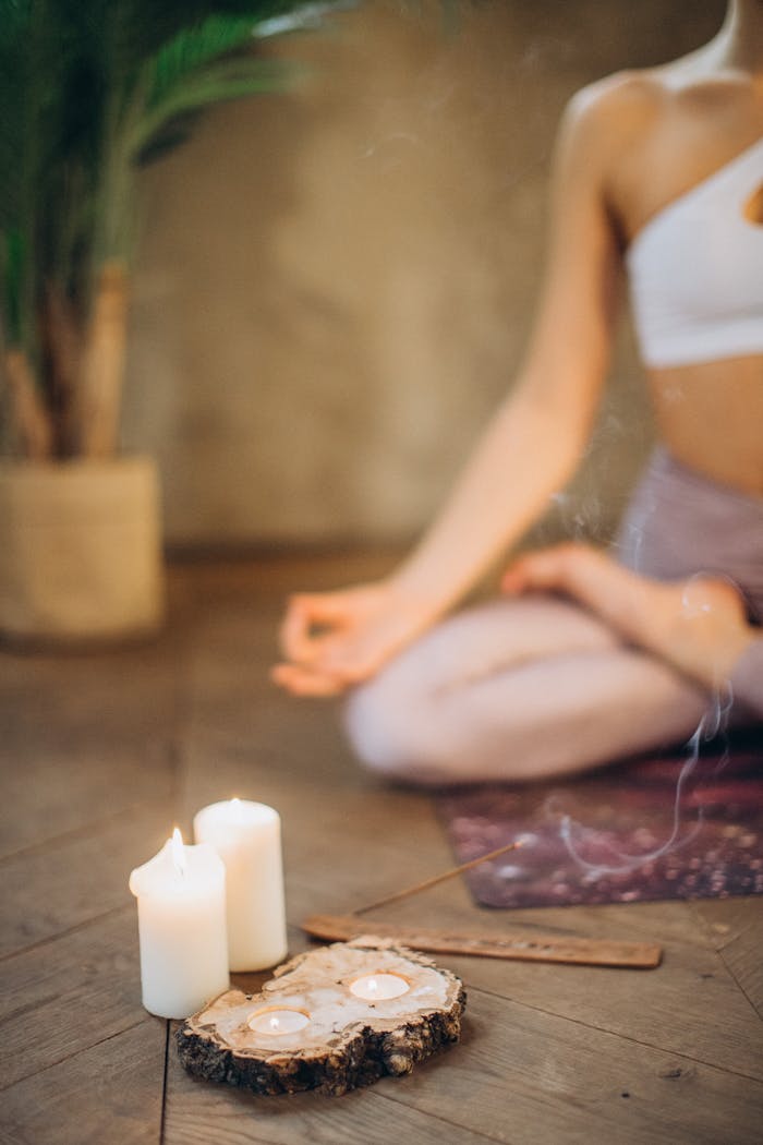 services-02 Woman practicing meditation in lotus pose with candles and incense, focusing on wellness and relaxation.